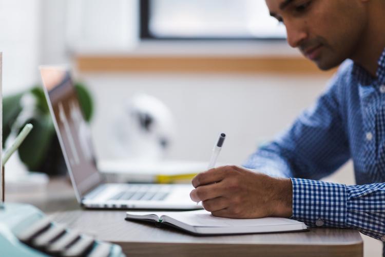 Man writing next to open laptop