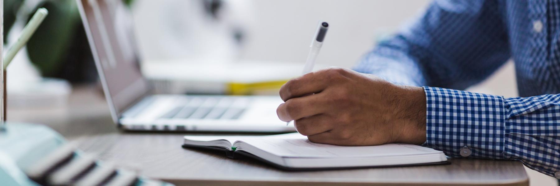 Man writing next to open laptop
